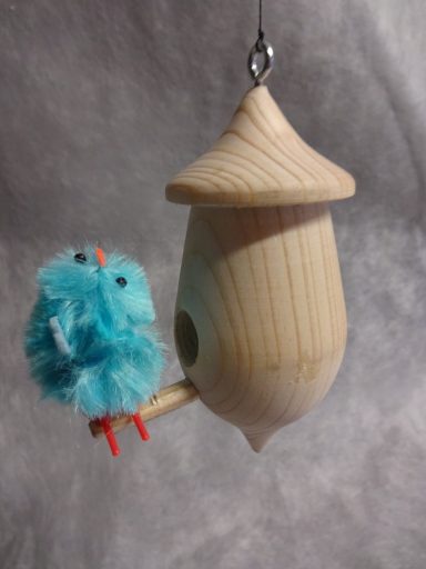 Houten vogelhuisje met pluchen vogeltje Houten vogelhuisje met een blauw, pluizig vogeltje dat erop zit.