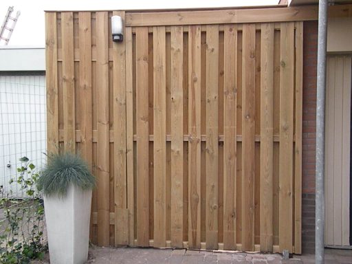 Houten tuin schuifdeur op maat Houten schutting met schuifdeur met verticale latten en een plantenbak met groen.