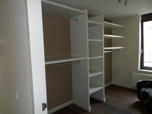 Witte inloopkast op maat Witte inloopkast met planken en hangruimte in een lichte kamer.