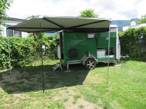 Caravan op maat Groene caravan met luifel op een grasveld, omringd door bomen en struiken.