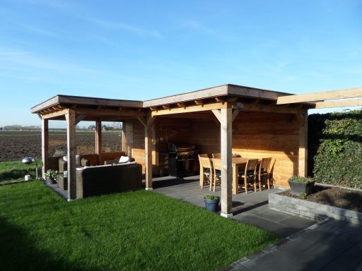 Houten tuinhuis op maat Houten tuinpaviljoen met zithoek en eettafel, omringd door gras en een blauwe lucht.