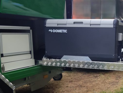 Uitschuifbare grote koelbox Uitschuifbare Dometic koelbox naast een uitschuifbare kookplaat van de buitenkeuken van een groene op maat caravan.