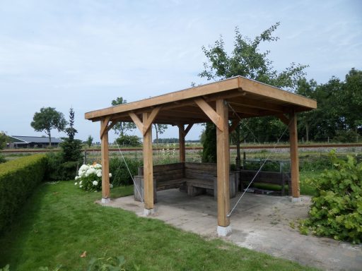 Houten prieel op maat Houten prieel met dak, omringd door gras en struiken.