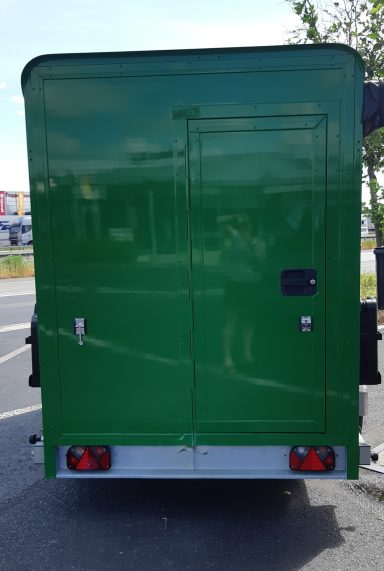 Ingang caravan op maat Groene caravan op maat met de ingang aan de achterkant, geparkeerd op een asfaltweg.