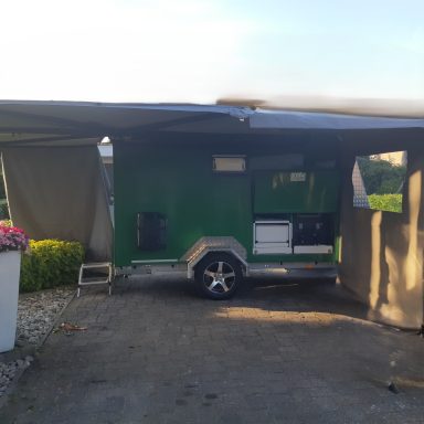 Zijkant inritsdoek luifel Groene caravan met luifel, gelegen op een parkachtige locatie.